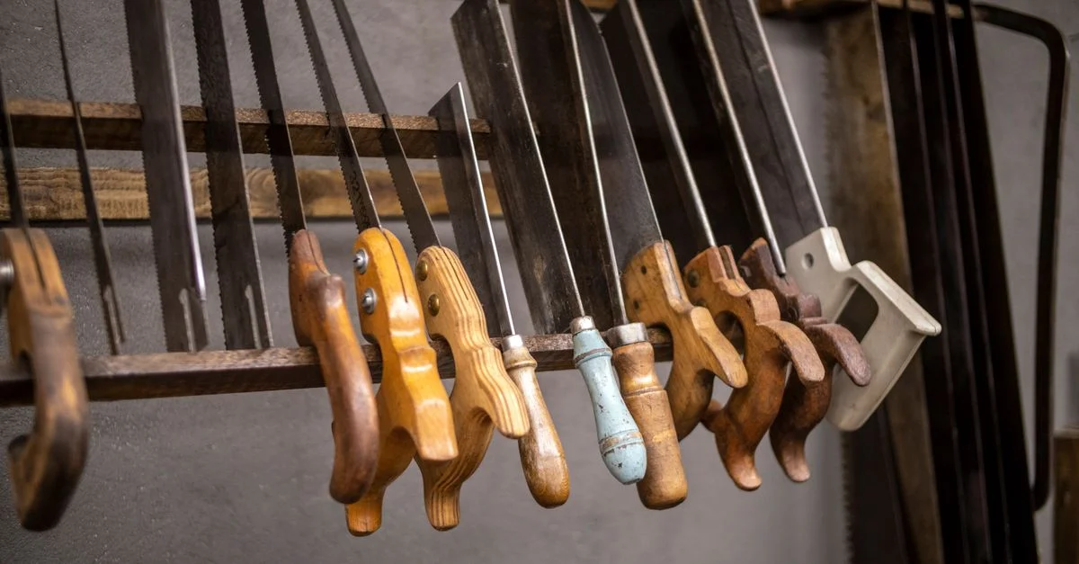 Assortiment de scies à main vintages avec des poignées en bois soigneusement exposées dans un cadre d'atelier.