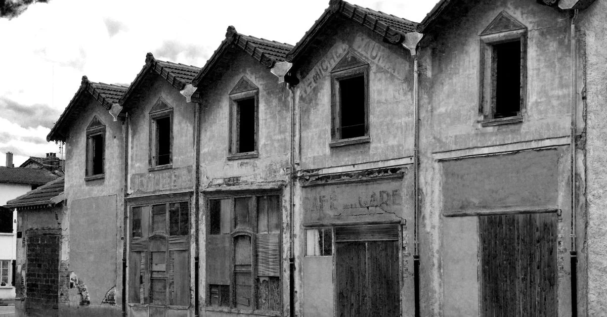 Photo en noir et blanc de bâtiments vintage abandonnés par temps nuageux, mettant en évidence la décadence architecturale.