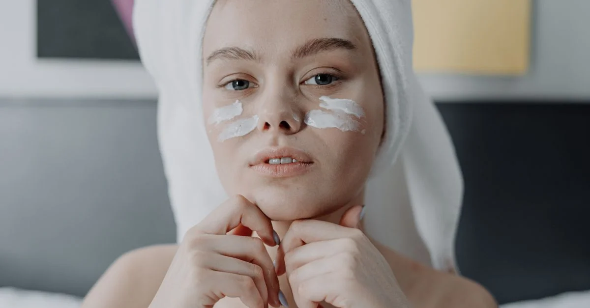 Portrait d'une jeune femme avec de la crème pour le visage, enveloppée dans une serviette, cadre intérieur.
