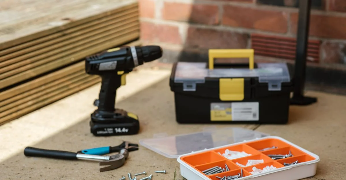 Un ensemble organisé d'outils incluant une perceuse, exposé à l'extérieur contre un mur en briques.