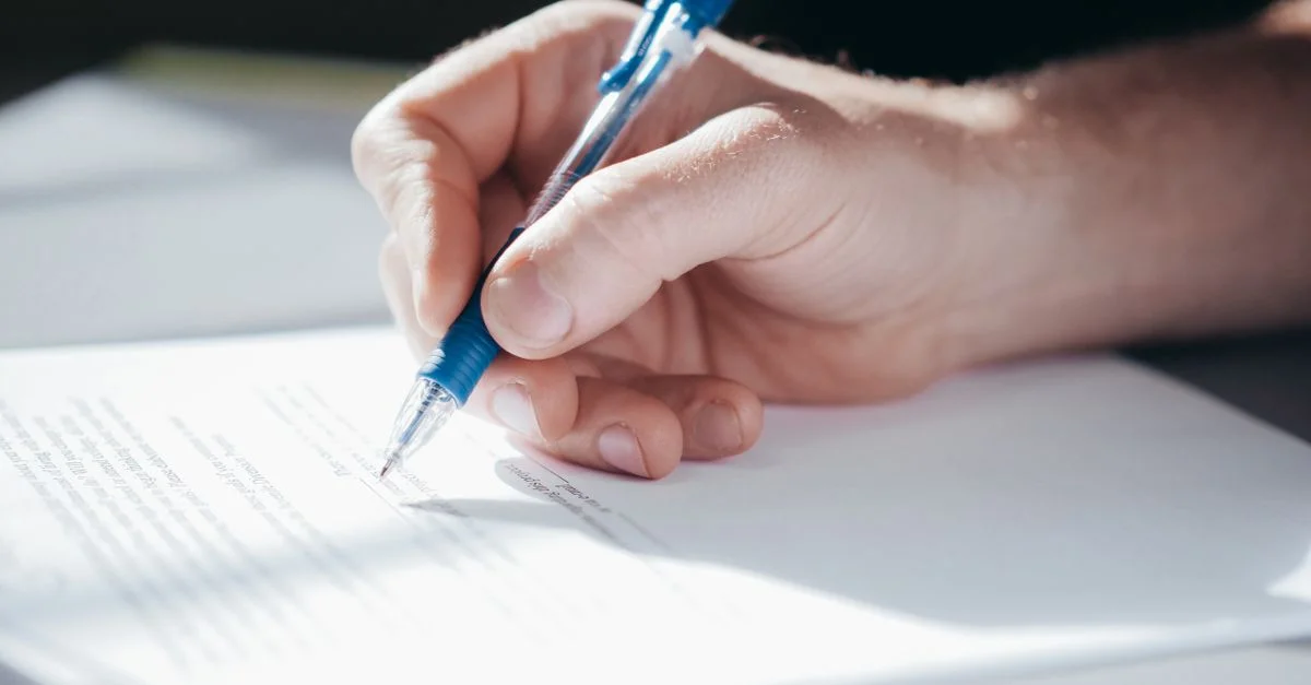 Un plan détaillé d'une main écrivant avec un stylo bleu sur une feuille de papier.