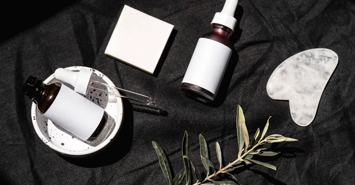 Vue de dessus de flacons de soins de la peau et de feuilles sur un tissu noir. Parfait pour des thèmes de beauté et de bien-être.