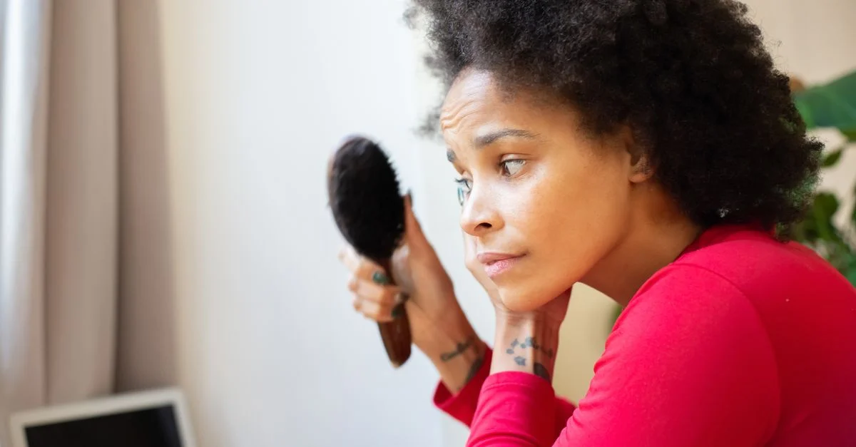 Une femme pensive aux cheveux afros se brosse les cheveux à l'intérieur, réfléchissant à un moment personnel.