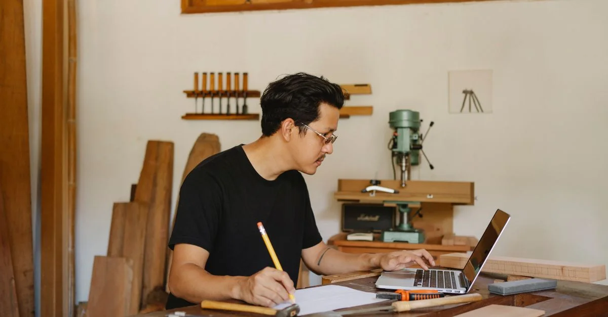 Un menuisier dédié concevant un projet de menuiserie sur un ordinateur portable dans son atelier.
